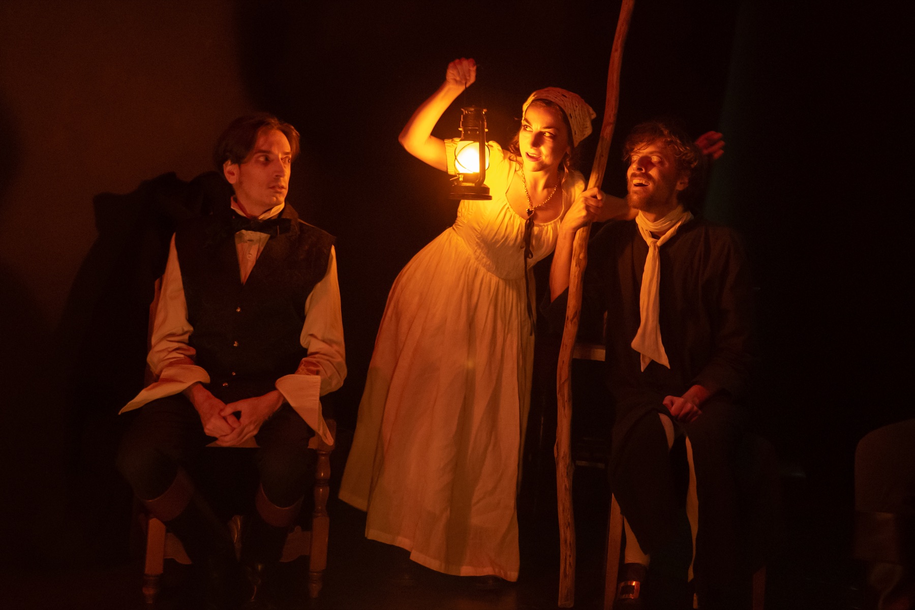 Tre interpreti lavorano in scena alla luce di una lanterna